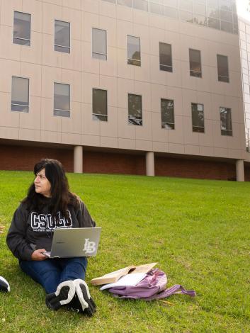 Students sit on grass while working on computers