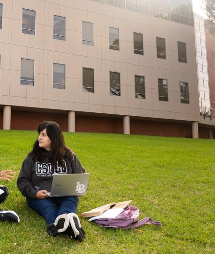 Students sit on grass while working on computers