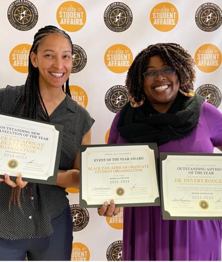 Two women hold up awards they received at an awards ceremony