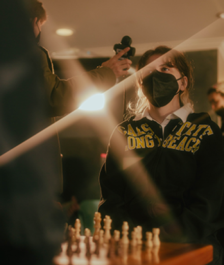 Student standing by chess set on film set with light meter in front of them