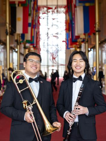 A trombone player and clarinet player stand in the Kennedy Center lobby smiling at the camera