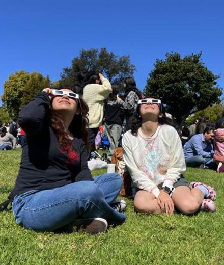 people sitting on grass watching eclipse with viewing glasses