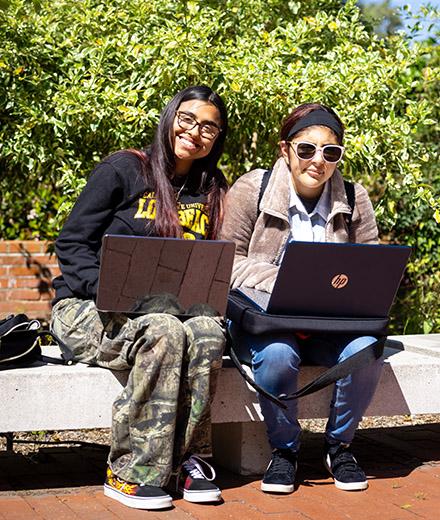 A student mentor with mentee, on a bench with laptops.