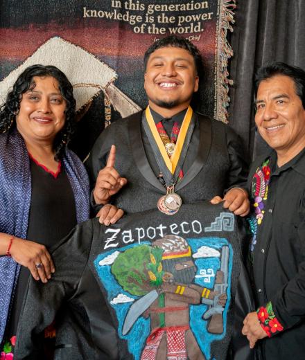 Native American graduate in cap and gown with parents.