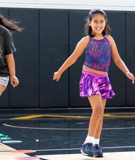 A child smiles as she skips in a gym