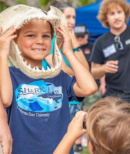 young child holding a large shark jaw up to their face and smiling