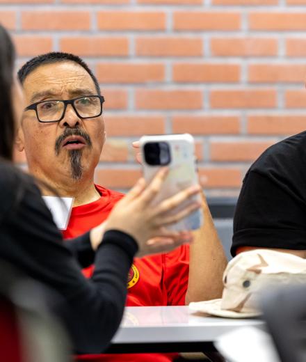 Three people talk at a table while one shows a phone