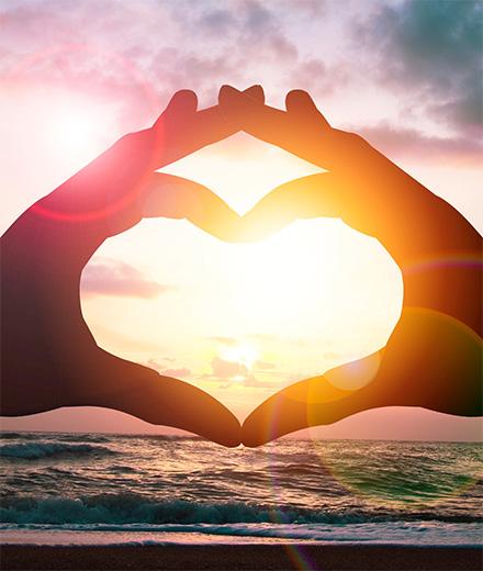 hands making a heart sign with sunrise in background