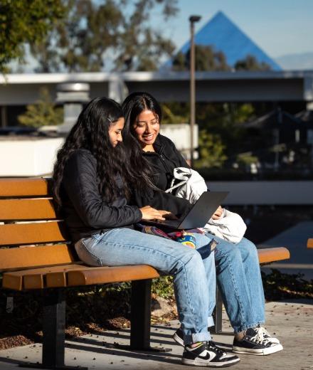 Two students sitting on a bench looking at one student's laptop