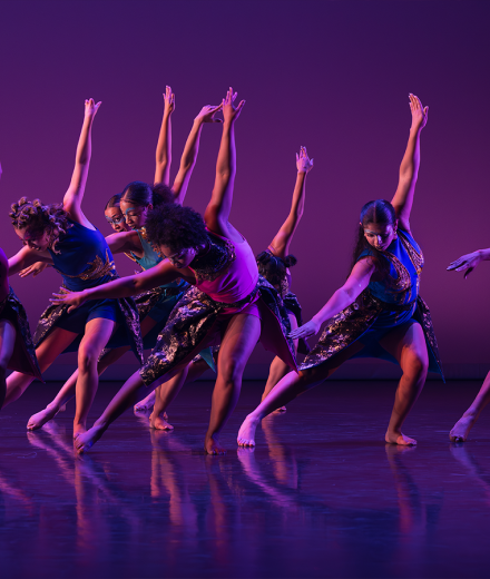 Dancers awash in purple light lean with hands outstretched