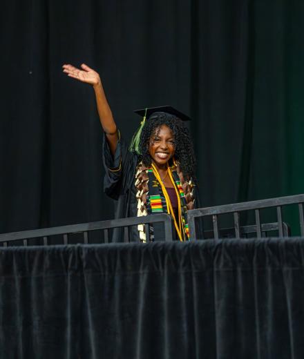 a graduate waving from the graduation stage