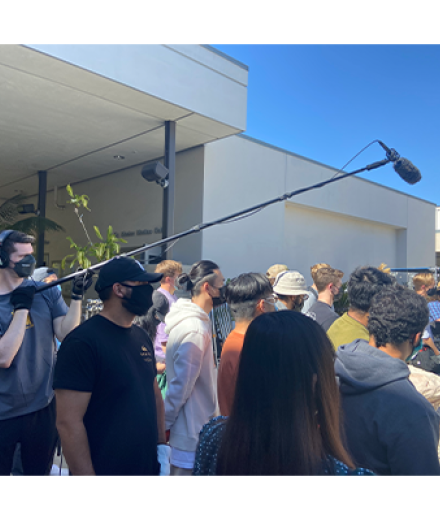 Boom operator holding mic over set surrounded by students 