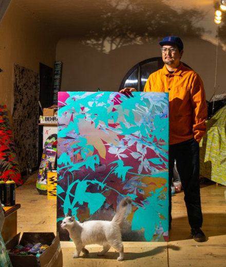 Artist Devin Tsuno standing in front of a painting