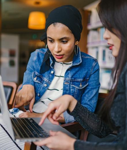 latinx woman and asian woman pointing and looking at laptop