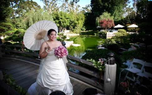 Wide angle capturing a bride holding a bouquet and parasol on the half moon bridge, the entire garden visible behind her.