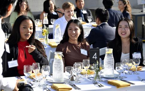 Three students smiling and having conversation after just being sat at the dinner table