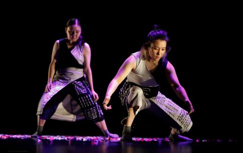 Two dancers on stage in gray and black jumpsuits with geometric embroidery patterns.