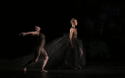 Two dancers on stage in sheer black dresses.