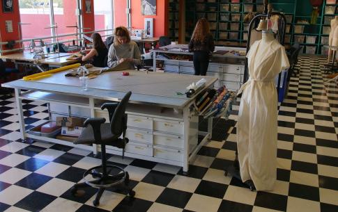 Students work in the Dance Costume shop. Black and white checkered floor with two large work tables being lit by a lot of natural light.