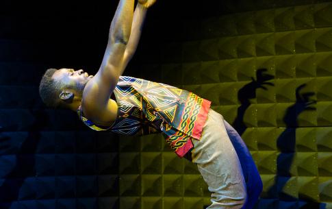 T performs on a dark stage illuminated by a spot light in grey sands and a colorful tank top.