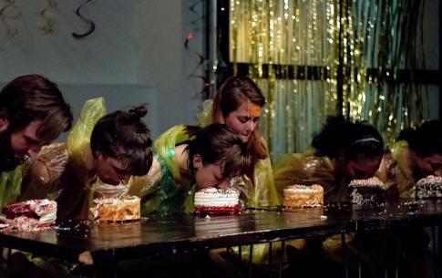 six people dressed in yellow rain ponchos compete in a cake eating contest.