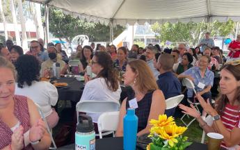 A group of people gather at tables under a tent at convocation event