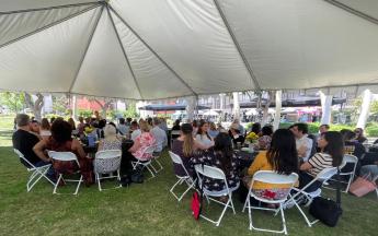 A group of people sit at round tables under a tent at a luncheon.