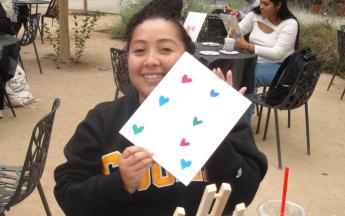 student sitting holding up their painting