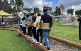 students working together to carry a wooden plank