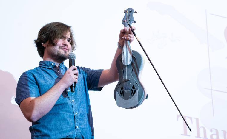 man holding up violin speaking into microphone