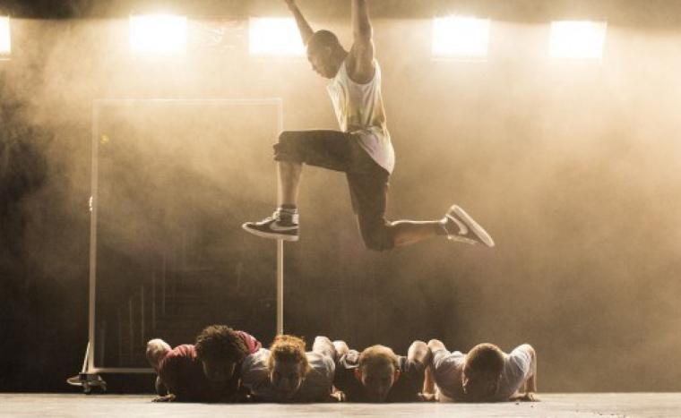On stage, a man jumps over four people laying down.