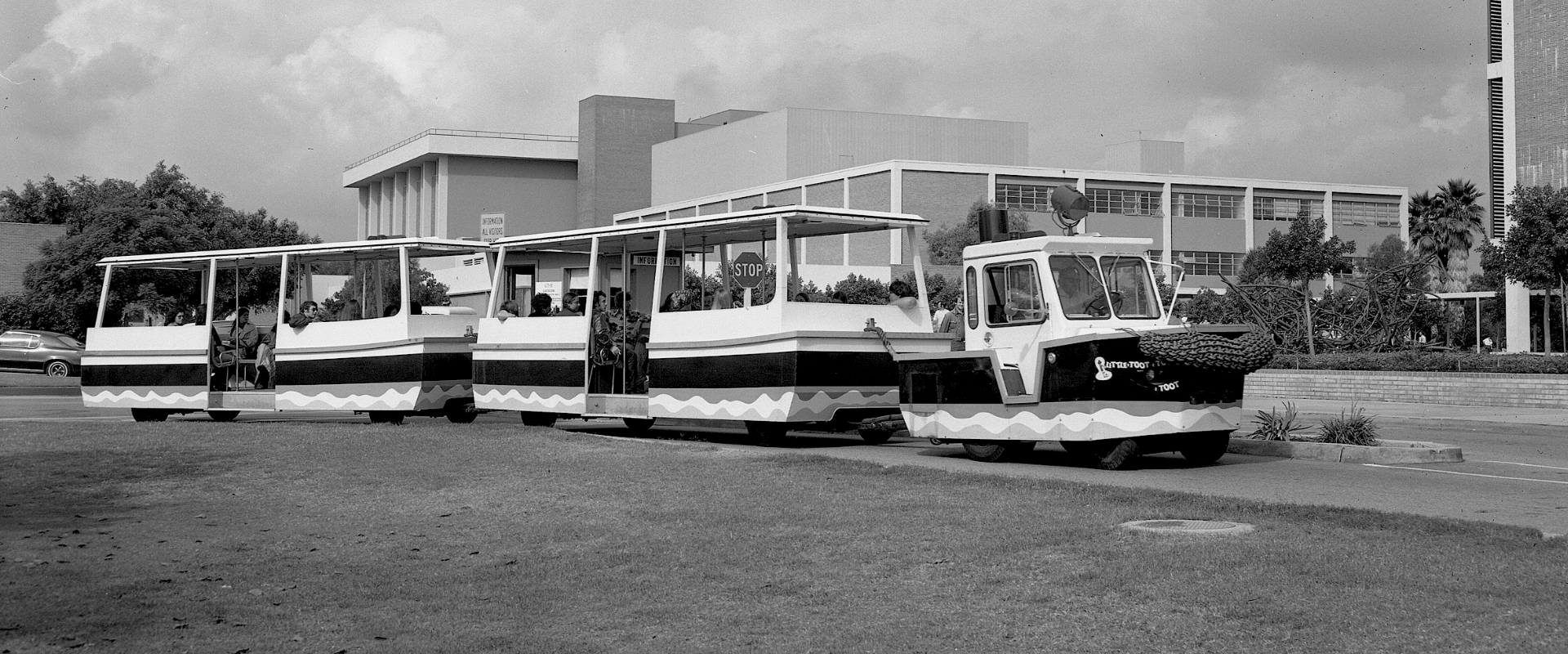 A small tram with several open-air cars carries passengers around a college campus.