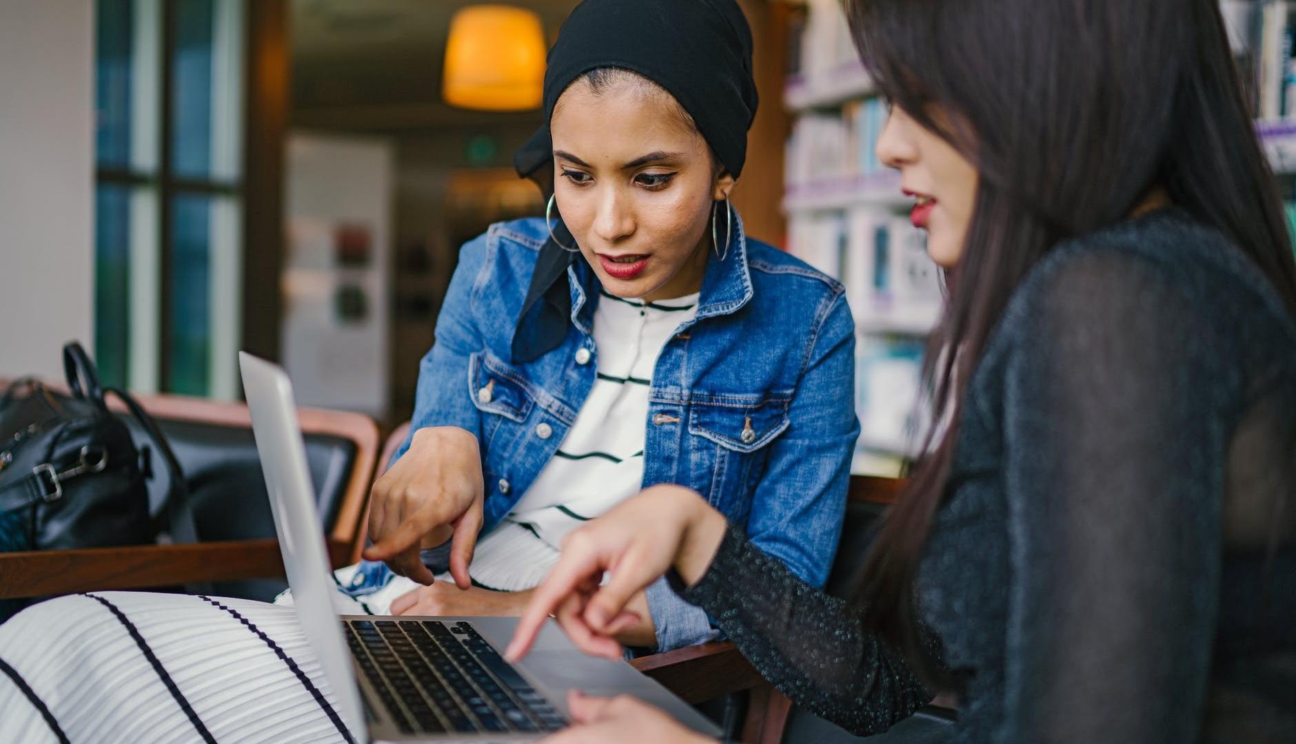 latinx woman and asian woman pointing and looking at laptop