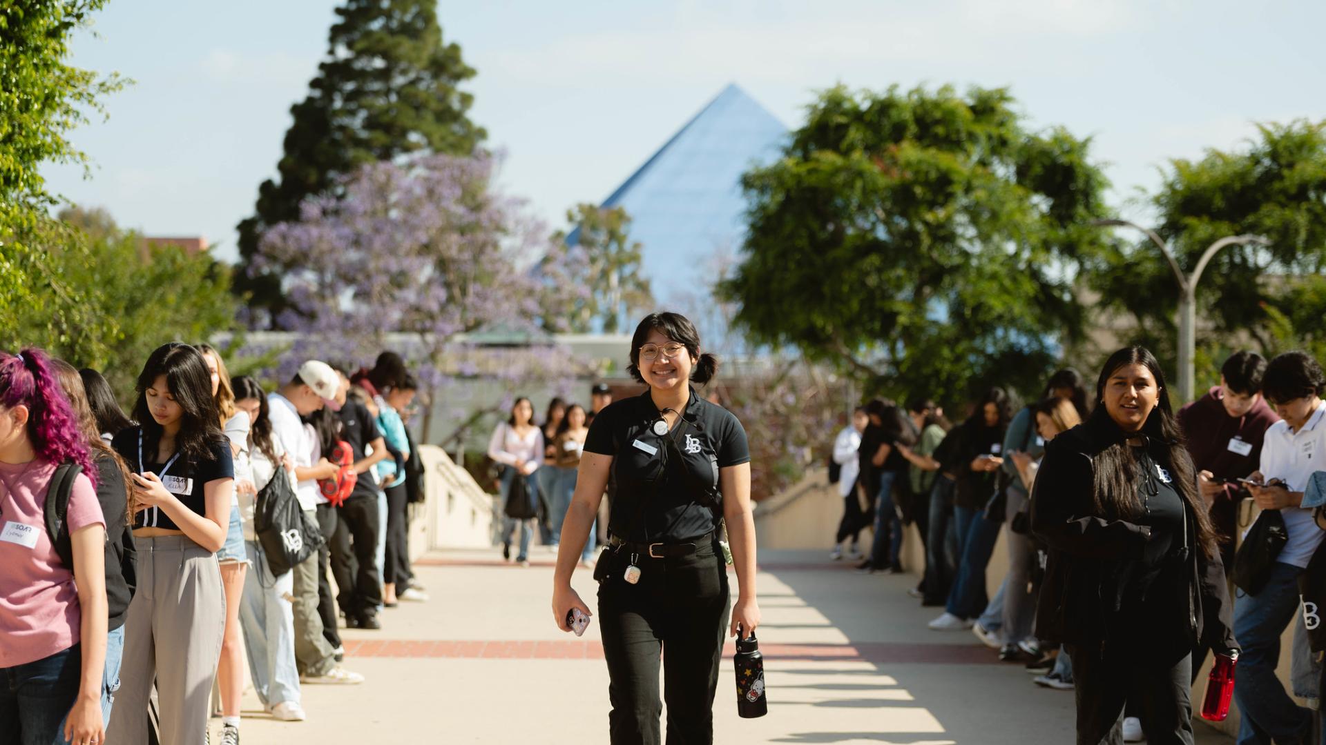 Students standing in line outdoors with a smiling student leader walking forward.