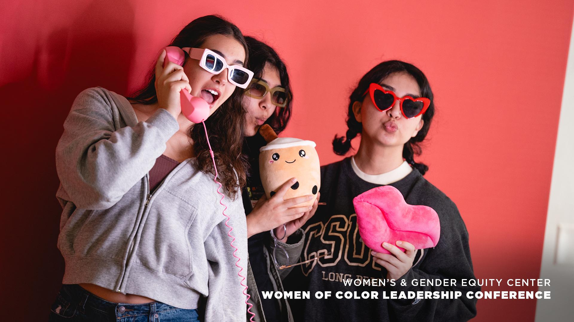 Three women posing playfully with props at leadership conference.