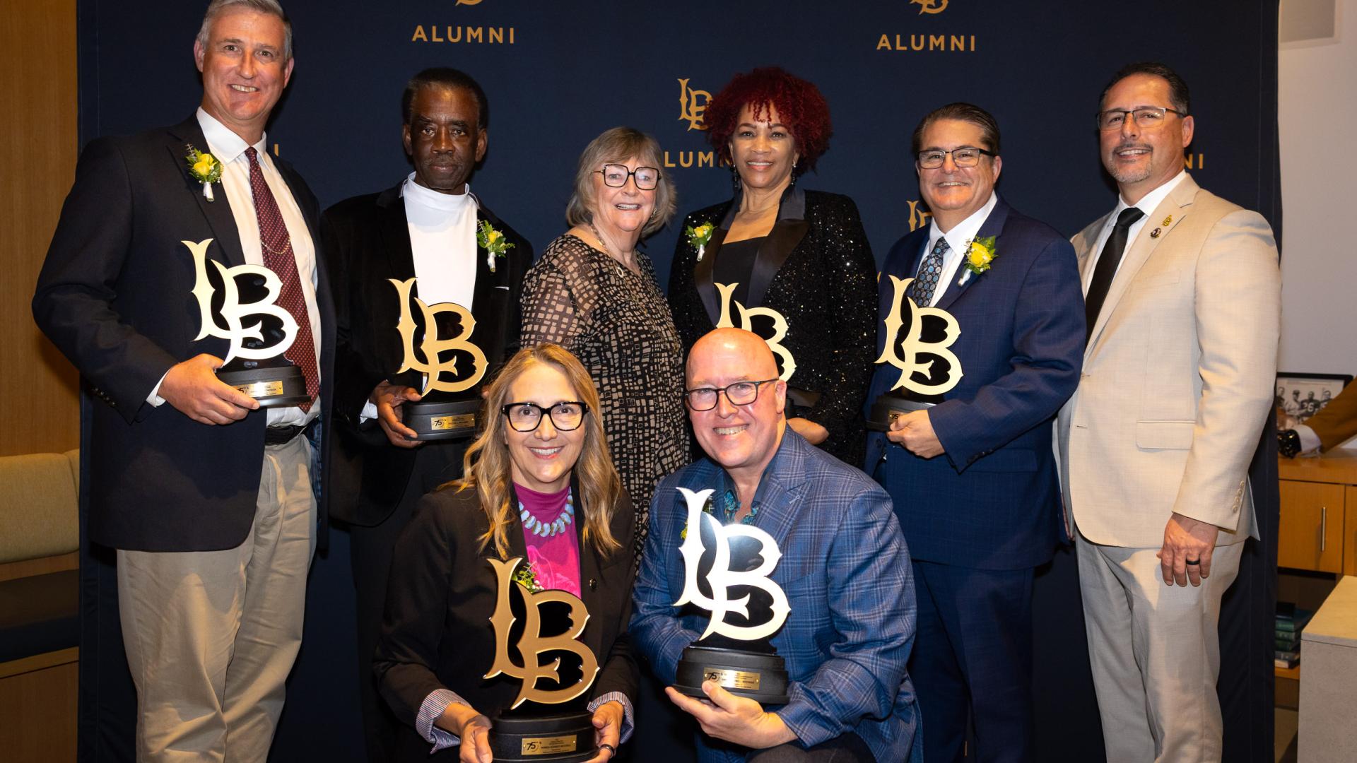 The 2025 Distinguished Alumni pose with "LB" shaped trophies while grouped with campus President Jane Close Conoley and Vice President Dan Montoya
