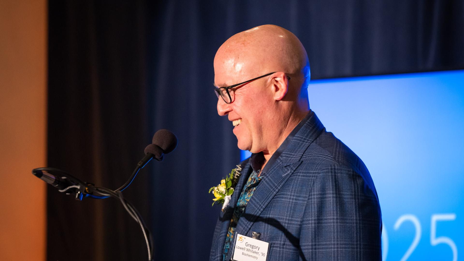 Distinguished Alumni honoree Gregory Lowell Whitaker smiles while standing at a podium