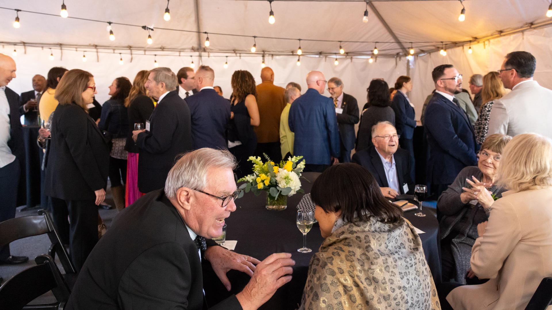A crowd socializes inside a tent before the 2025 Distinguished Alumni Awards