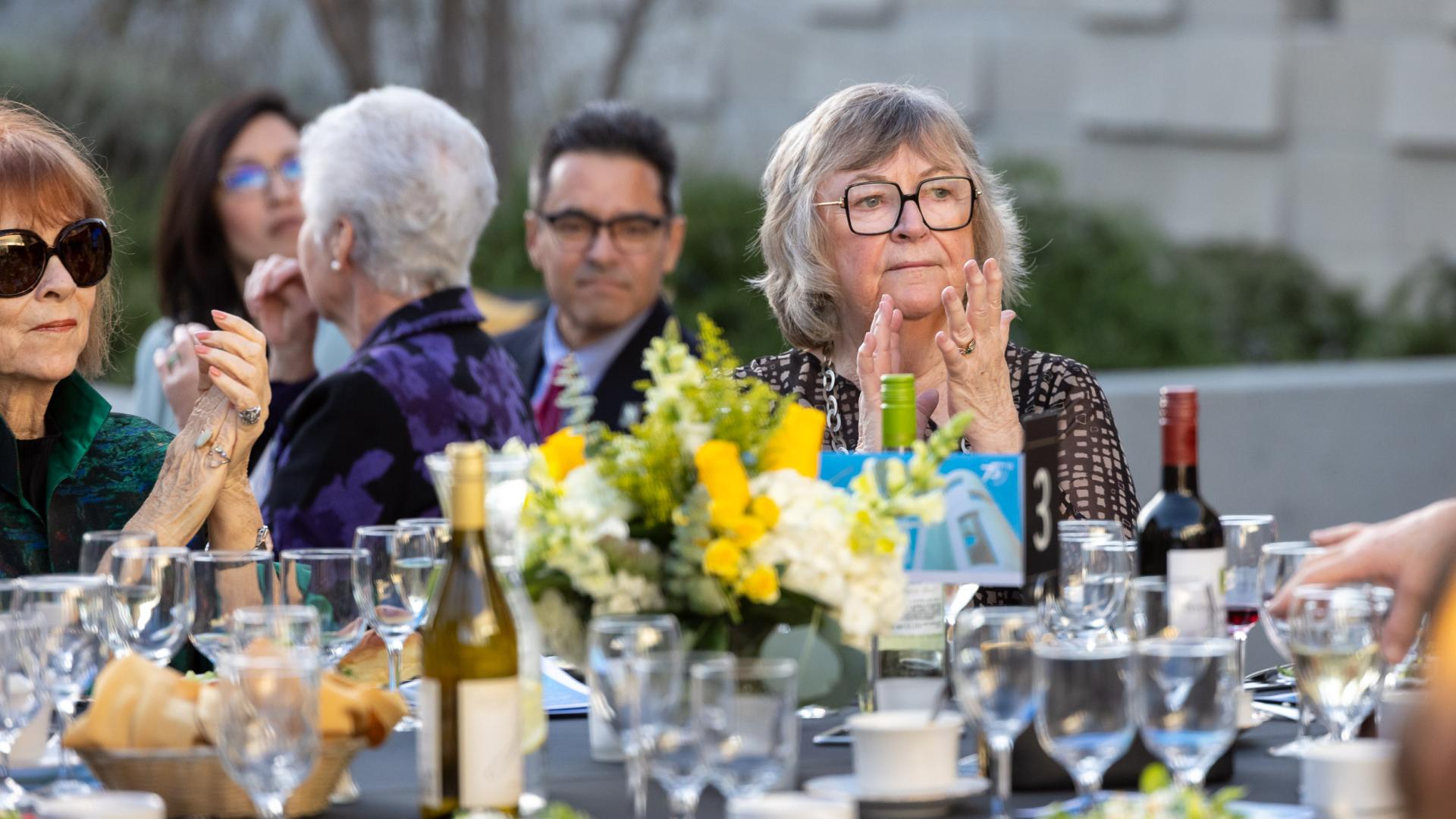 Campus President Jane Close Conoley applauds while seated at a table
