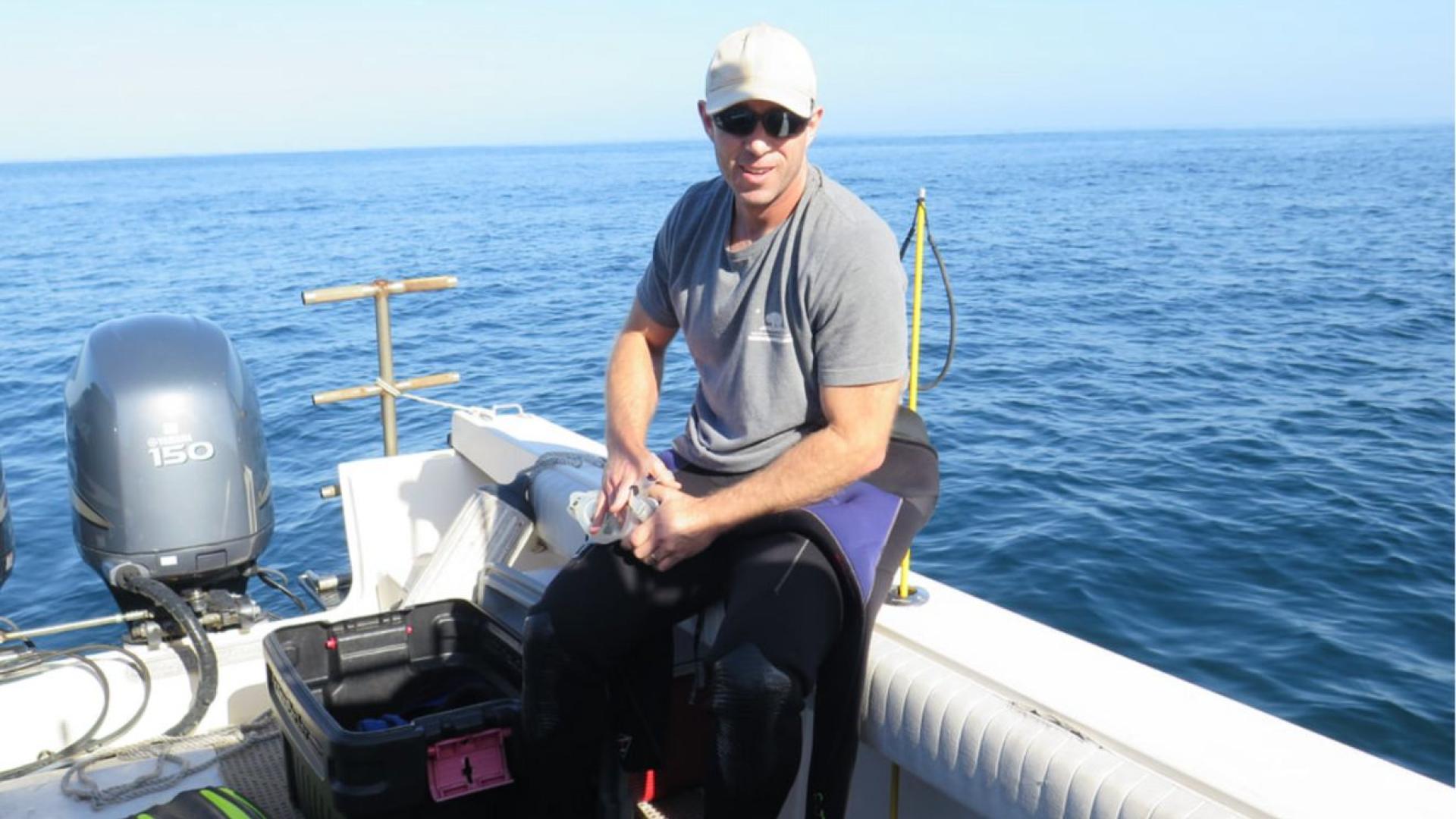 A man sits on the side of a small motor boat on the ocean