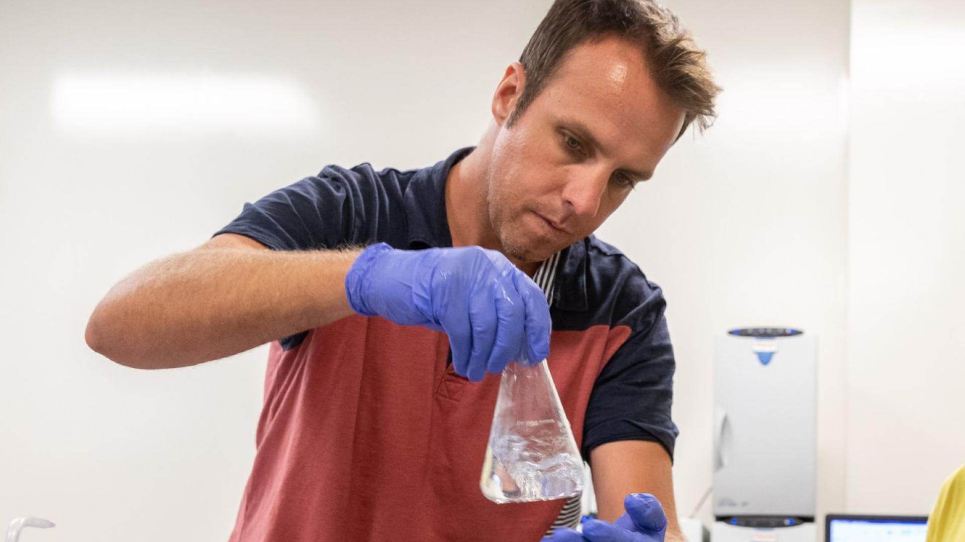 A man in latex gloves looks at a beeker