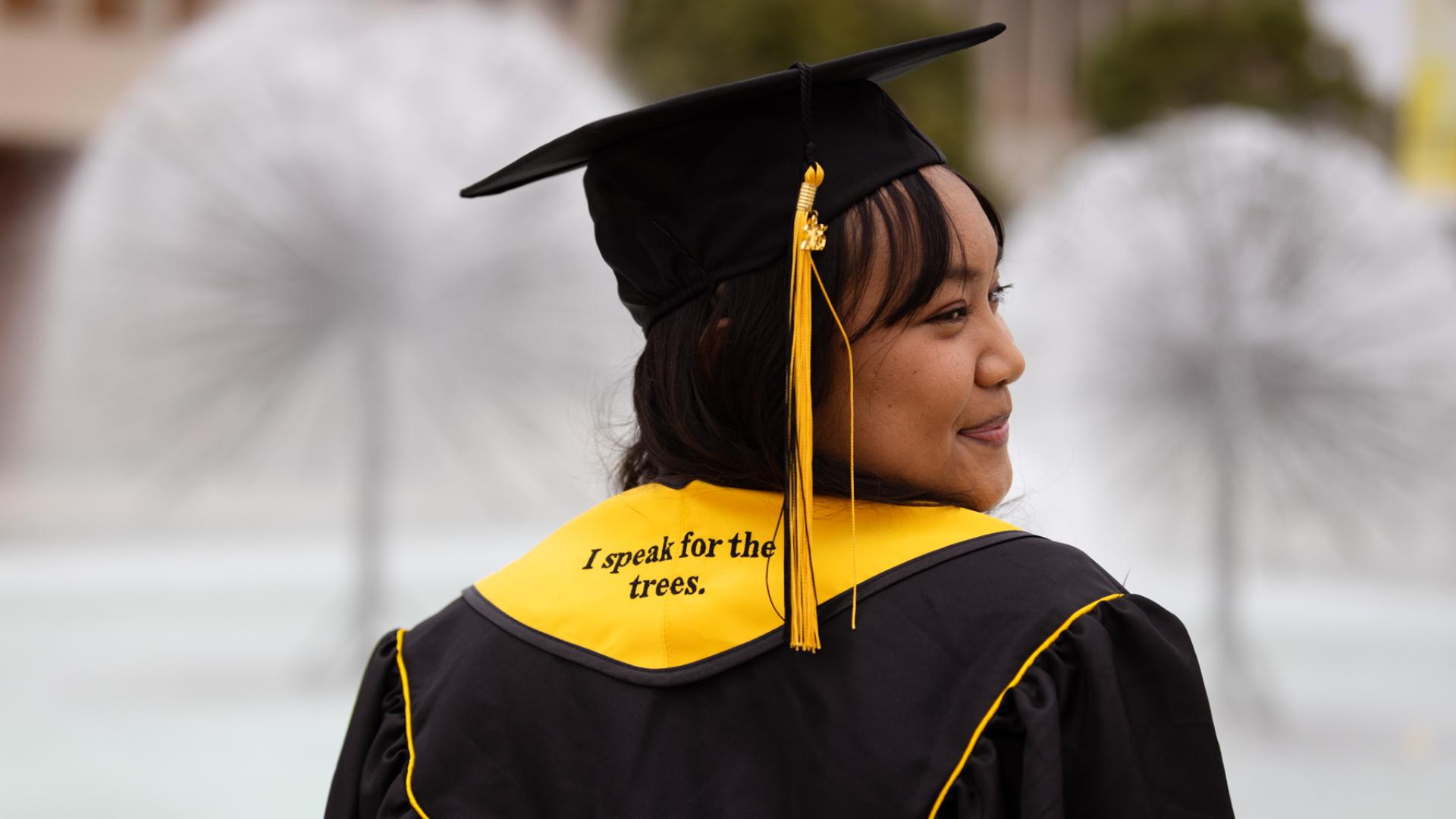 Student sitting in front of water fountain with graduation cap
