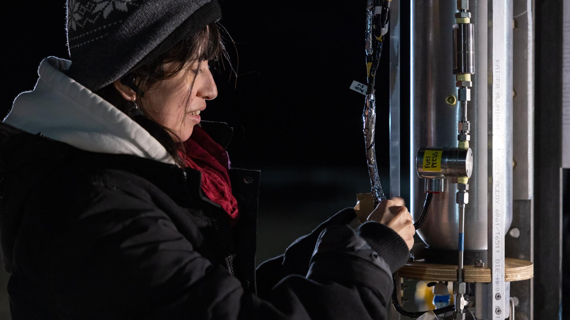 A CSULB student checks wiring on a rocket system at night