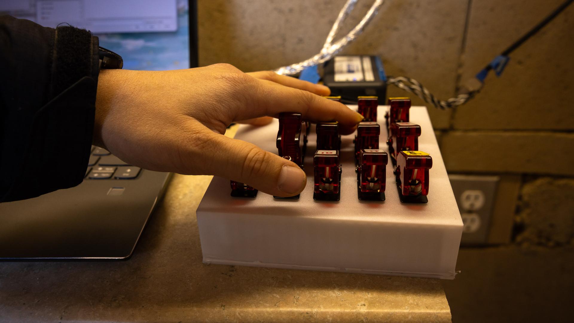  hand operates red toggle switches beside a laptop during testing