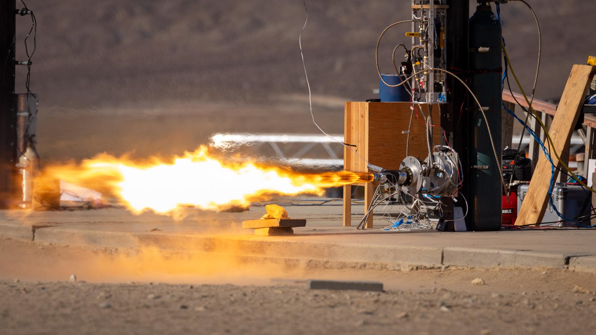 A rocket engine fires on a test stand surrounded by wires and tanks