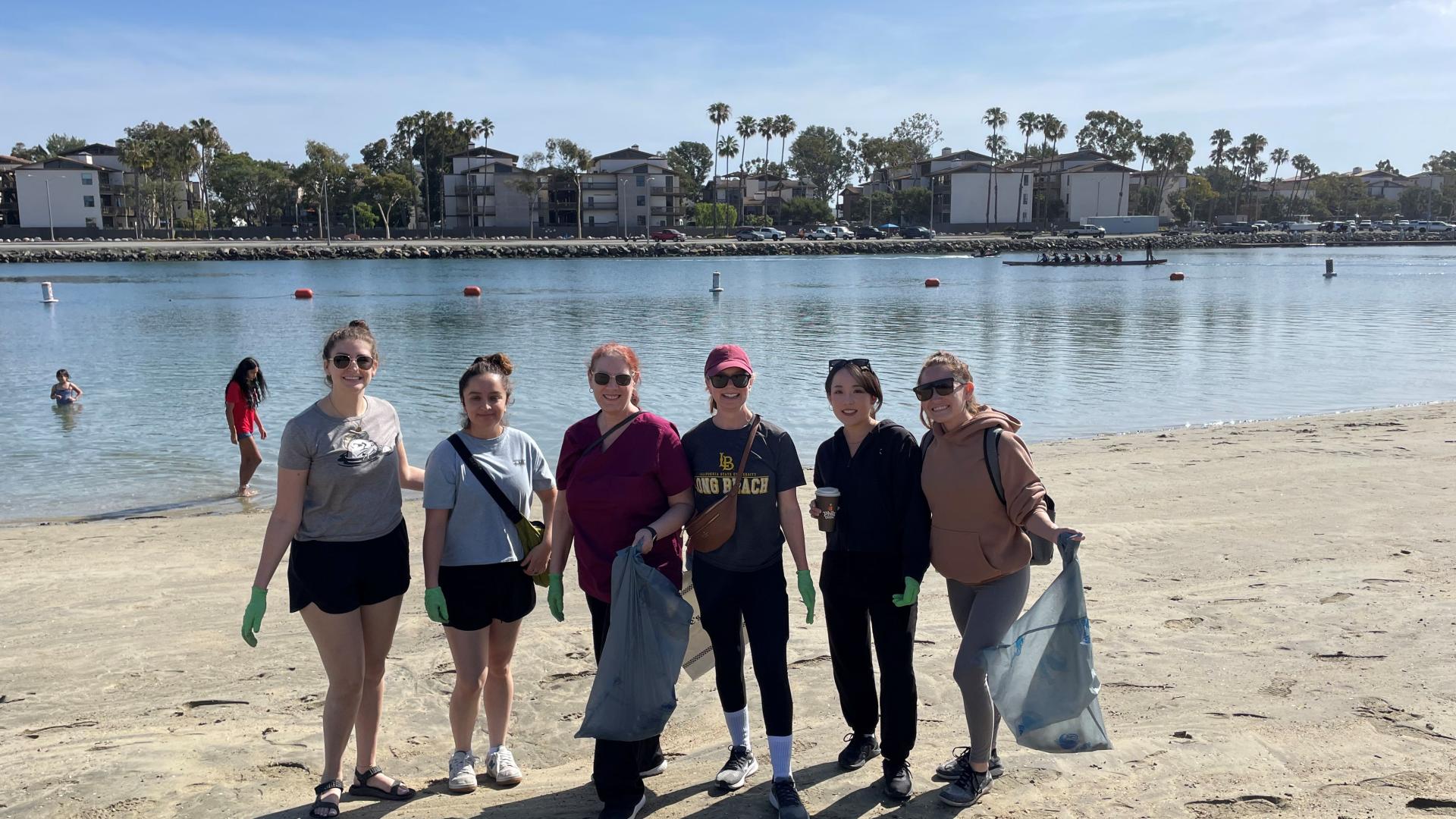 Group of volunteers wearing gloves and holding trash bags during a beach cleanup near water
