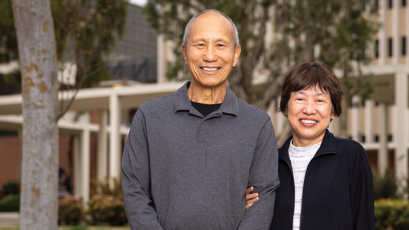 A couple stand smiling in front of building