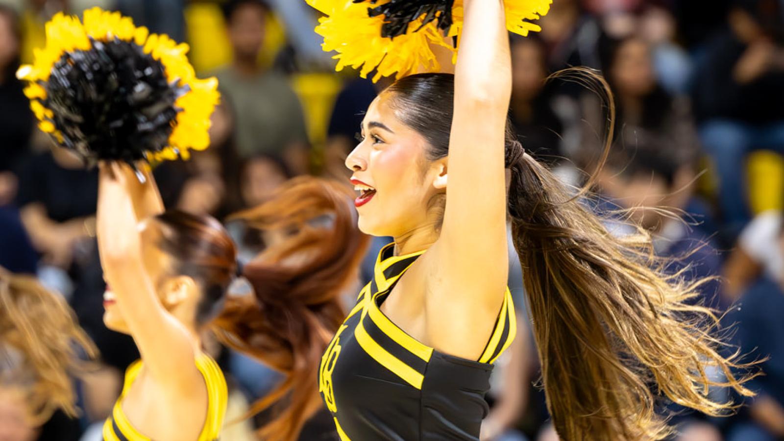 A group of people raise pom-poms in front of an audience at an indoor arena.