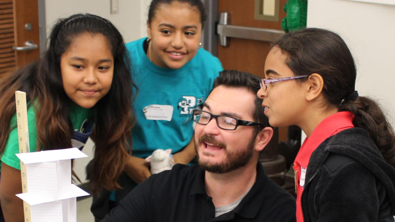 teacher measing an index card tower as young students watch in excitement