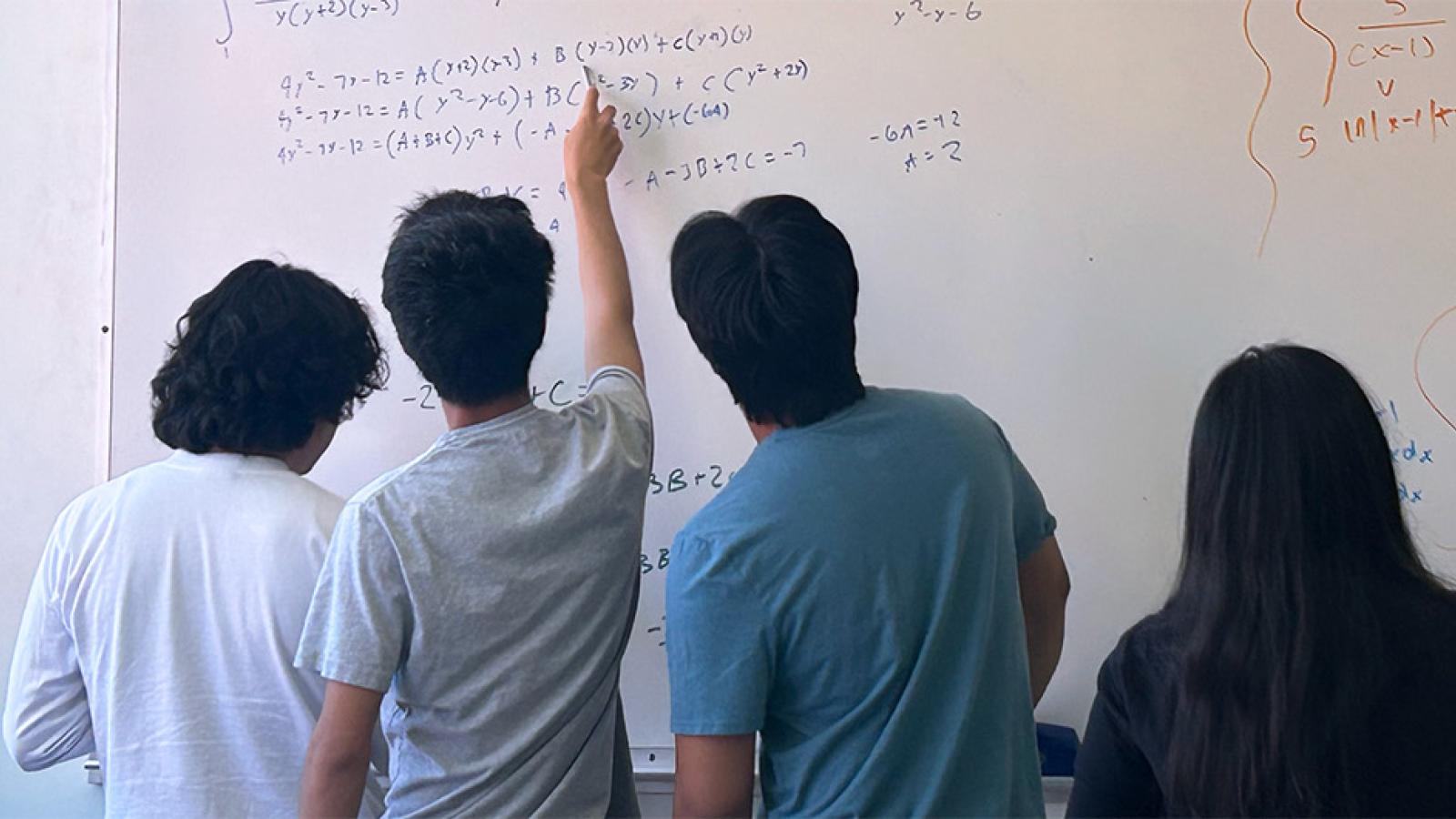 students completing math problems on a whiteboard